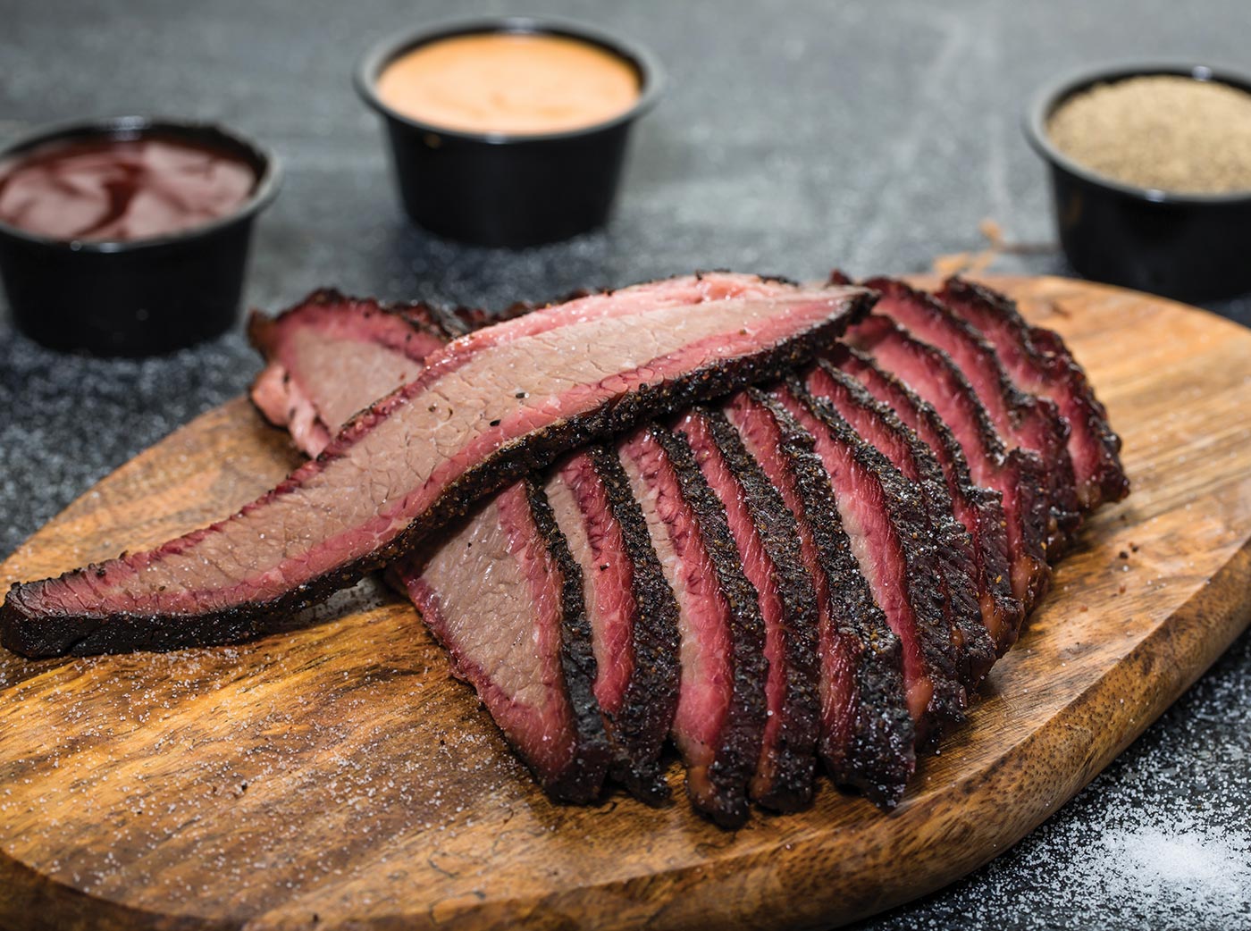 Beef brisket smoked and sliced thin on wooden cutting board with dipping sauces