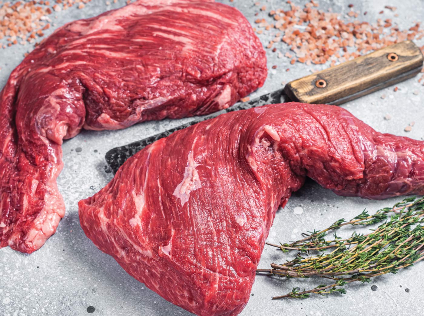 Two raw beef tri tip steaks on a cutting board